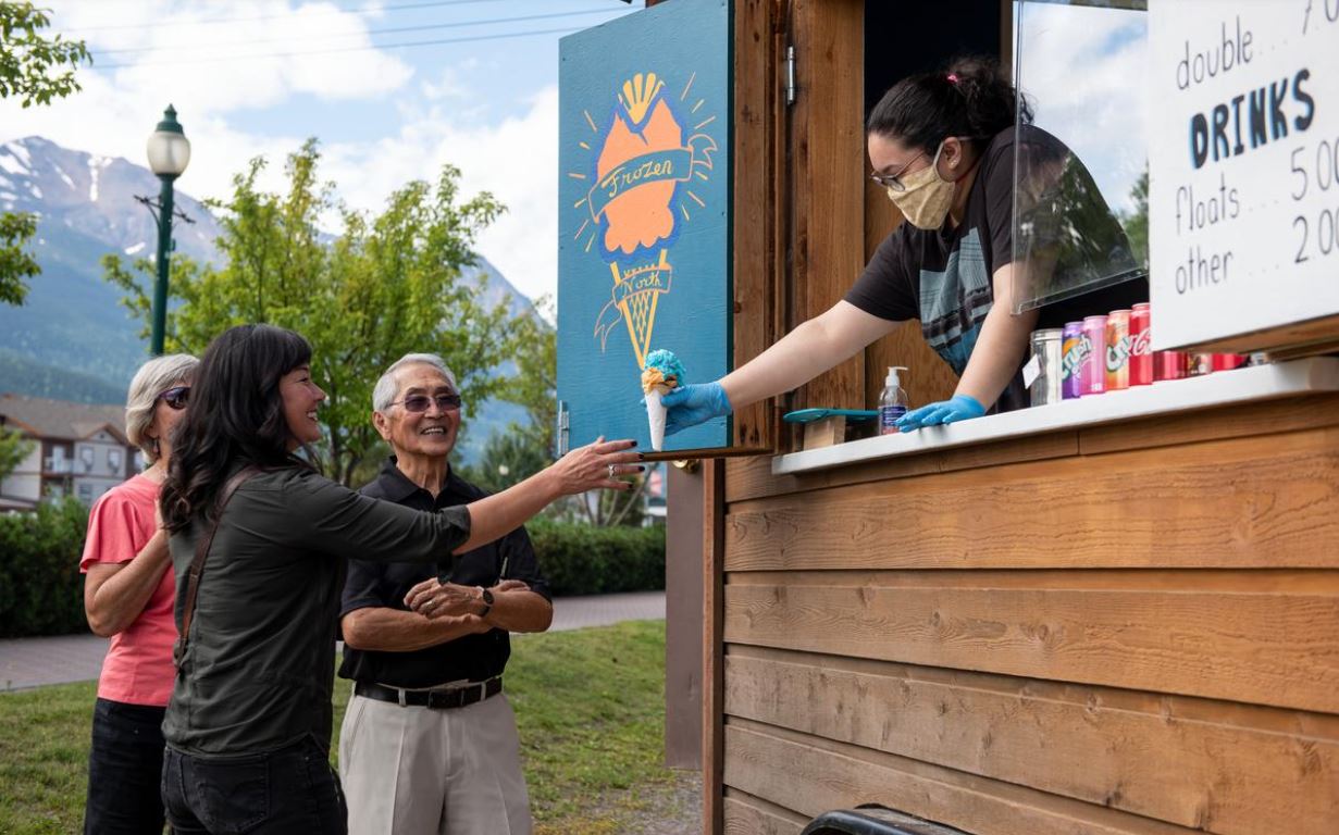 Image dans un stand de crème glacée, une employée donne un cornet de crème glacée à un groupe de clients